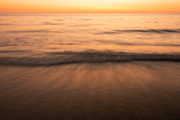 Naklejka na ściany i meble Long exposure of waves on beach at sunset