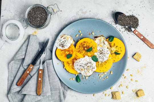 Sliced persimmon with yogurt, chia seeds, brown sugar, pine nuts and fresh mint
