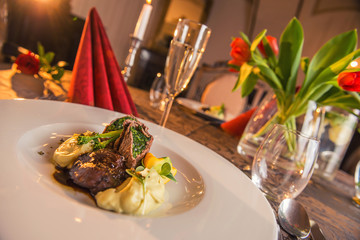 baked beef with baby patizone, sauce and spinach served on white plate with flowers and champagne, romantic time on valentines day