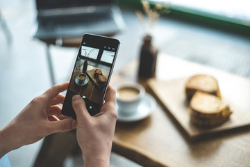 Woman making photo of her fresh food in cafe using cellular