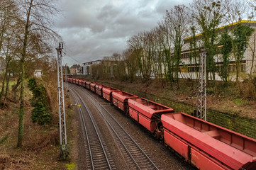 Empty train wagons are moving on the rail passing through the city and there are trees on the both sides 