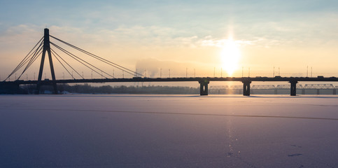big beautiful concrete suspension bridge in winter sunset / sunrise. ice on the river. background.