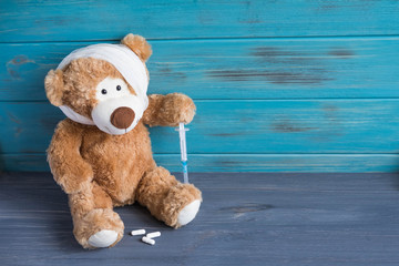 Obraz premium Toy bear with a bandaged head rewound. The basis for the banner associated with the health of children. Children health. Syringe and pills