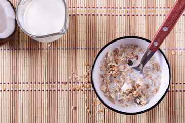 Healthy and tasty granola breakfast with coconut pieces and milk on a straw napkin, top view