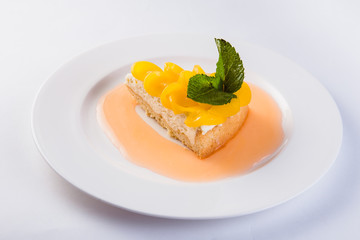 Peach cheesecake on a white plate on a light background (close)
