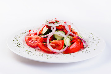 Greek salad, dressed with olive oil on a white plate on a light background (close)