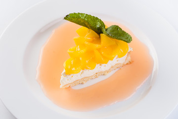 Peach cheesecake on a white plate on a light background (close)
