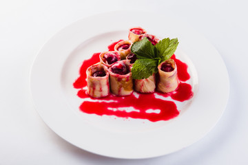 rolled pancakes stuffed with berries called white plate on a light background (close)