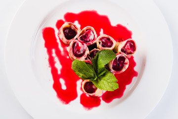 rolled pancakes stuffed with berries called white plate on a light background (close top view)