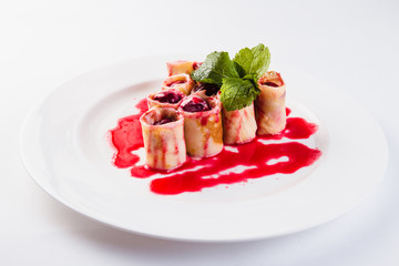 rolled pancakes stuffed with berries called white plate on a light background (close)
