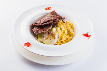 Tagliatelle with beef on a white round plate on a light background