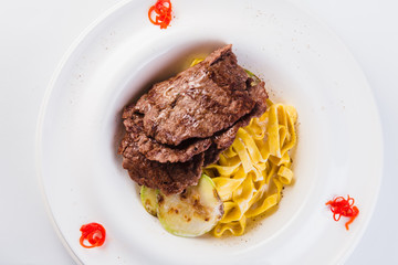 Tagliatelle with beef on a white round plate on a light background. Close top view