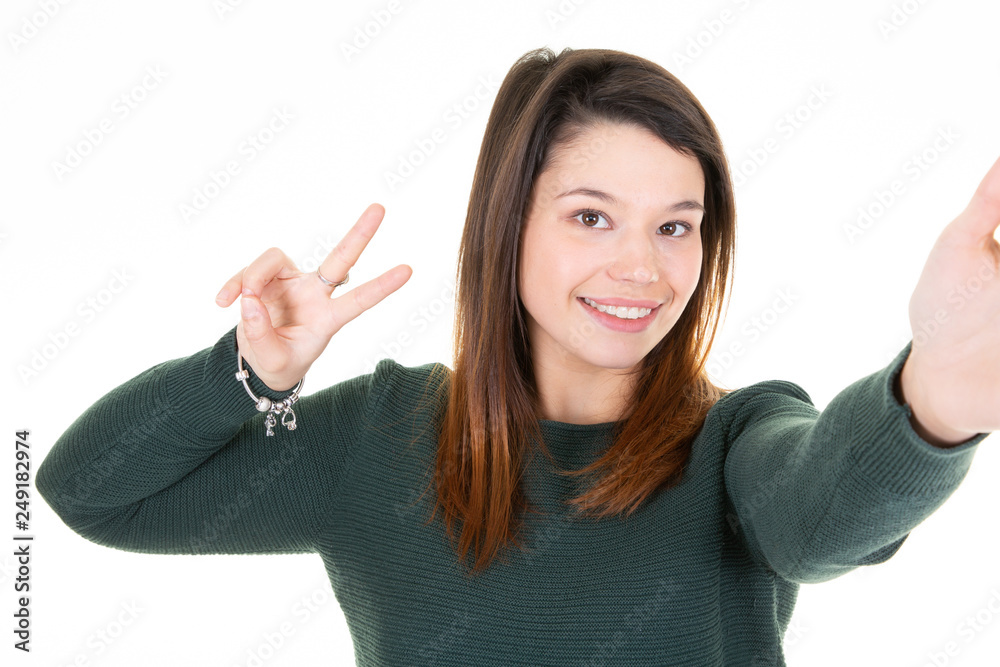 Wall mural Young woman in green sweater making selfie and showing peace gesture