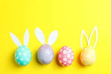 Decorated Easter eggs with cute bunnies ears on yellow background. Space for text