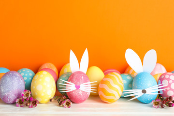 Decorated Easter eggs and cute bunny's ears on table against color background. Space for text
