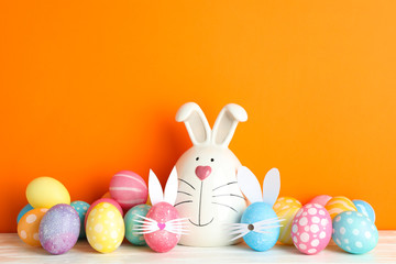 Decorated bunny and Easter eggs on table against color background. Space for text