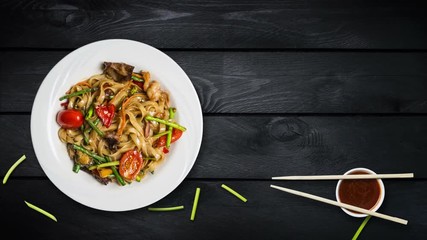 Rotating udon stir fry noodles with seafood and vegetables. Decorated with fresh bean sprouts and chopsticks in a white plate on black wooden background. Top view with the copy space for your text