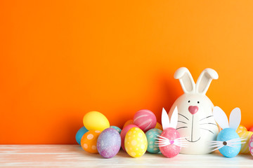 Decorated bunny and Easter eggs on table against color background. Space for text