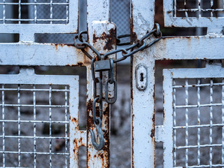 Image of old chain with padlock and white iron gate