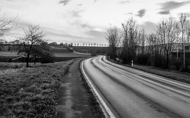 Empty curved road leading to the horizon in the countryside, monochrome. Bad Friedrichshall, southern Germany. Dramatic scene.