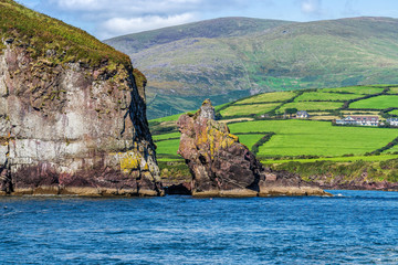 Green fields and high cliff with mountains in a distance &ndash; view from sea