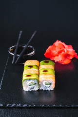  sushi rolls with wasabi, soy sauce, ginger, chopsticks and teapot on black stone background