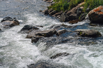 Big boulders in mountain creek close-up. Rapids of fast river with copy space. Foamed water stream. Fast flow near wet stones. Background of clean water waves. Natural texture of shiny stream of creek