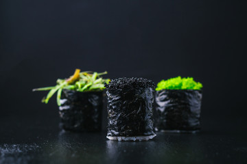  sushi rolls with wasabi, soy sauce, ginger, chopsticks and teapot on black stone background