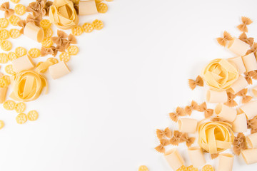 An overhead photo of different types of pasta, including spaghetti, penne, fusilli, and others, flay lay on a white background with a place for text