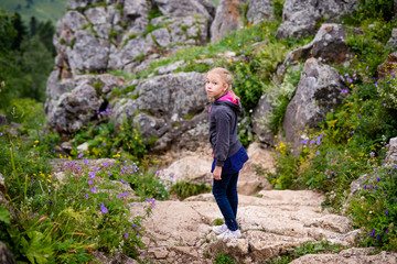 Cute blonde girl in the mountains wearing warm gray jacket