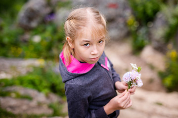 Cute blonde girl in the mountains with flowers wearing warm gray jacket