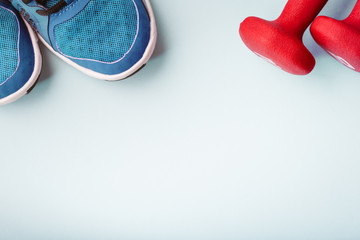 Sneakers and dumbbells on the solid blue backdrop. Keep fit athletic and healthy sports concept
