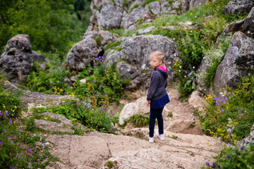 Cute blonde girl in the mountains wearing warm gray jacket