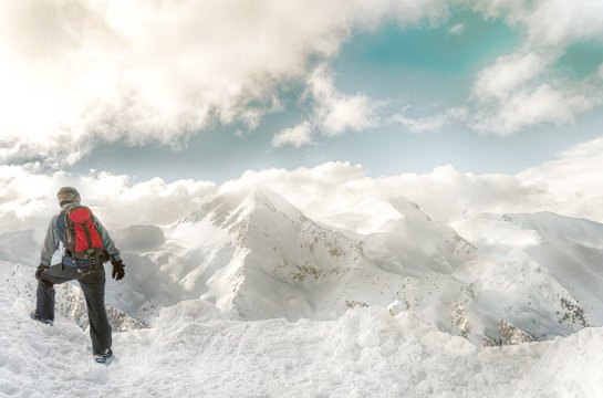 Snowboarder stay with snowboard in hands sits on big rock on mountains backdrop. Bansko, Bulgaria