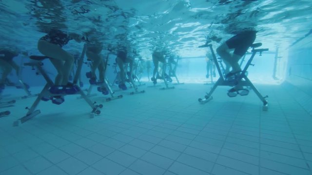 Underwater view of people aqua biking in a swimming pool slow motion