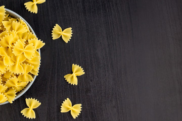 Top view of black background with italian raw farfalle or pasta in bowl with copy space