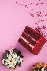A piece of delicious red velvet cake and eclairs on a pink background.