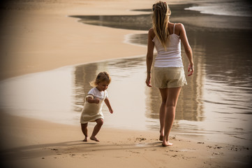 blond mother and toddler daughter walking in the sand of an empty beautiful beach during summer