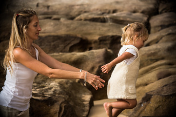 blond mother taking care of her baby daughter in the rocks of a beautiful beach 