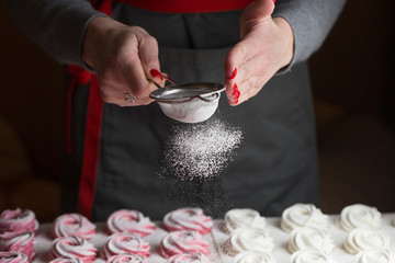 Obraz na płótnie Canvas process of making marshmallow. Close up hands of the chef with metal sieve sprinkling zephyr with Powdered sugar at pastry shop kitchen. confectioner sprinkles sugar powder confectionery