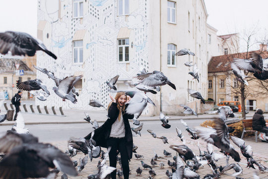 Positive young blondie girl in the city fedding a flock of pigeons