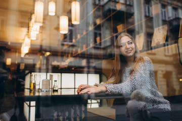 View from the street. Young beautiful blonde girl sitting in a cafe in the city center