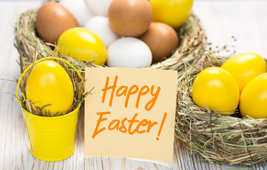 Yellow colored Easter eggs in nest on wooden background, selective focus image. Happy Easter card