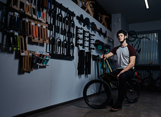 Professional BMX rider sitting on his bike next to a stand with BMX parts in a bicycle shop