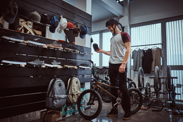 Teenage BMX rider standing with his bike, choosing new sneakers in a shop.