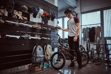 Teenage BMX rider standing with his bike, choosing new sneakers in a shop.
