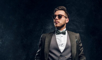 A stylish man in sunglasses dressed in an elegant suit against a dark textured wall