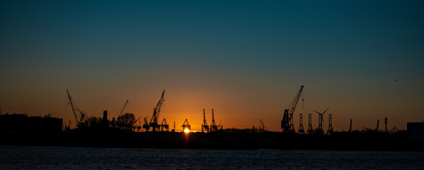 Panorama of industrial cityscape with metallurgical and chemical plants and big . Smoke pipes emissions. A background of an orange-colored sky. Industry city. A moment of a sunrise with big water