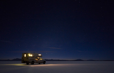 Illuminated campervan on salt lake under starry sky