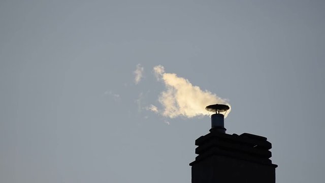 Footage of a chimney of the condominium heating system. The low rays of the winter sun enhance the puffs of smoke that increase and decrease depending on the engagement of the boiler.
